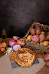 Typical Spanish potato omelette, served at the table with the necessary ingredients for the recipe, potatoes, eggs, onion and garlic