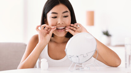 Young asian woman using dental floss looking in mirror