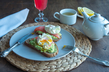 Breakfast. Sandwich with avocado, salmon and poached egg, tea, red orange juice