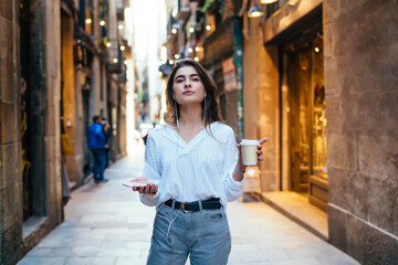 Stylish woman with takeaway coffee and smartphone on aged street