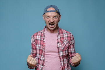 Caucasian man threatens someone, he clenched his fists showing his strength and shouts furiously. Blue background.