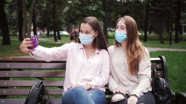 Beautiful happy girls students taking photos by smartphone. Women in medical masks making video call during quarantine of coronavirus.