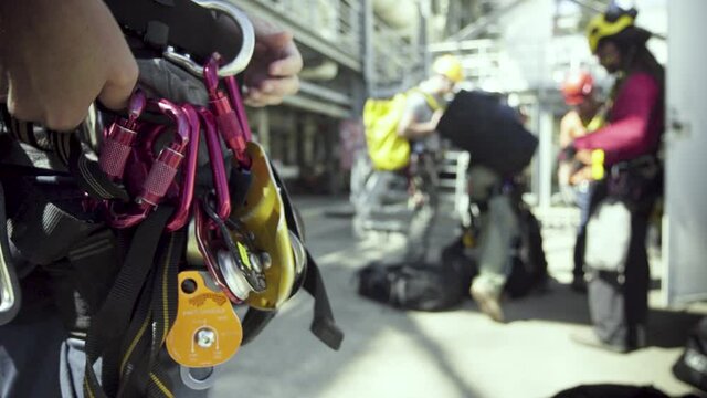 A climbing crew adjusts their harnesses and safety gear before climbing an industrial building.