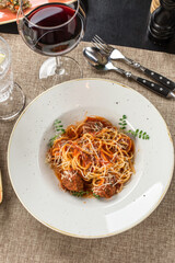 spaghetti with meatballs and tomato sauce and glass of red wine on the table at restaurant