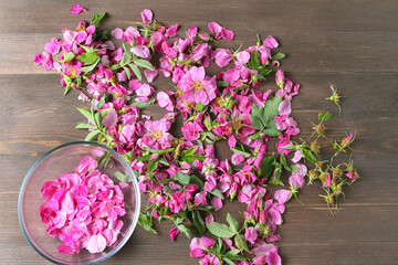 rose petals in a glass bowl on the background of lying pink flowers for drying on wood table