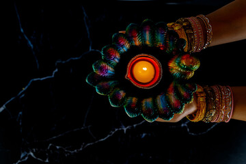 Happy Diwali - Woman hands with henna holding lit candle isolated on dark background.