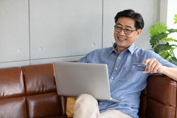 senior asian man using laptop computer for shopping online and paying with credit card