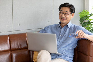 senior asian man using laptop computer for shopping online and paying with credit card
