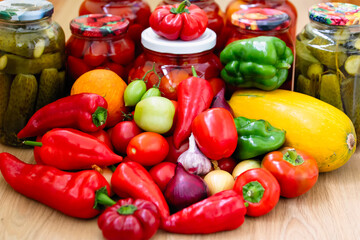 Canned cucumbers and tomatoes in jars on a wooden background. Lots of fresh peppers and tomatoes. Preservation of vegetables for the winter at home.