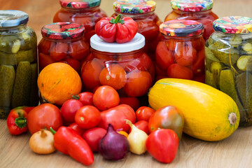 Canned cucumbers and tomatoes in jars on a wooden background. Lots of fresh peppers and tomatoes. Preservation of vegetables for the winter at home.