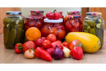 Canned cucumbers and tomatoes in jars on a wooden background. Lots of fresh peppers and tomatoes. Preservation of vegetables for the winter at home.