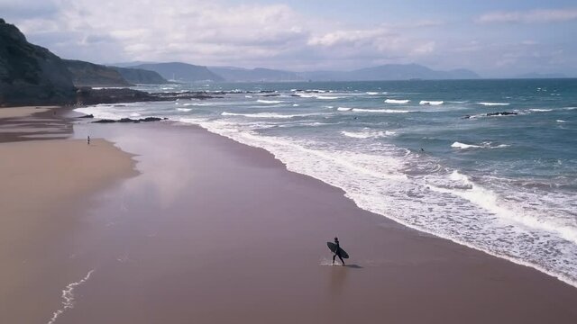 Smooth drone view on Sopelana Beach as a surfer comes out of the water with his board. 4K ProRes