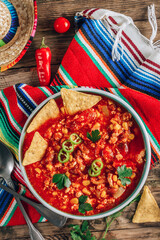 Chili Con Carne in bowl with tortilla chips on wooden background. Mexican cuisine. Top view. Vertical photo