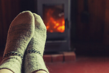 Feet legs in winter clothes wool socks at fireplace background. Woman sitting at home on winter or...