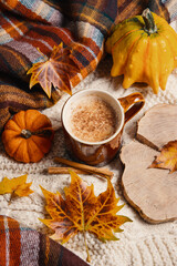 Pumpkin spiced latte or coffee in cup and dry leaves on knit jumper. Autumn or winter hot drink.