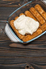 tiramisu dessert cooking - Traditional Italian Savoiardi ladyfingers Biscuits and cream in glass baking dish on wooden background