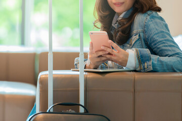 Woman in hotel lobby using mobile phone and Female traveler sitting with travel suitcase while...