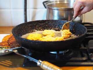 The process of frying natural dietary pumpkin and millet pancakes in a pan on the stove. An elderly woman's homemade food.Country style.
