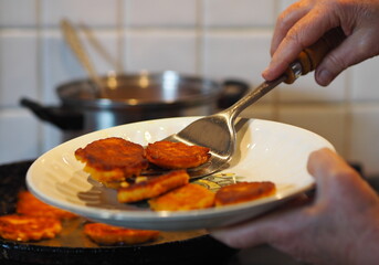 An elderly woman prepares natural diet pancakes from pumpkin and millet in a frying pan on the stove.Home cooking, rustic style.