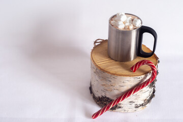 A cup of hot chocolate with marshmallows and Christmas lollipops on a hemp. On a light background