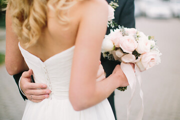 Bride holds bouquet in her hand, and groom hugs her waist. Selective focus. Newlyweds concept.