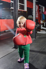 Little girl in red boxing gloves in the gym.
