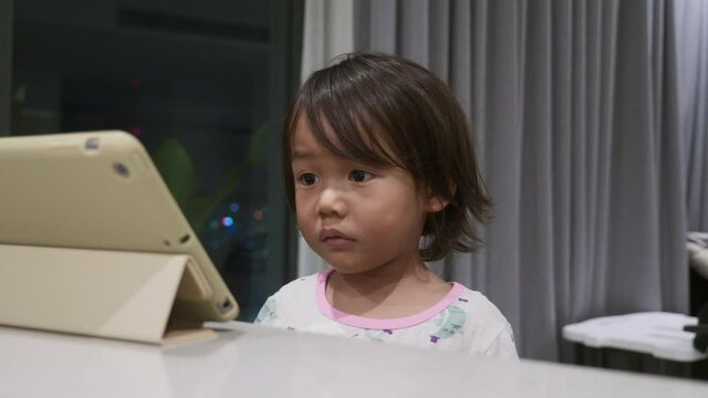 Wideshot of a toddler watching a video on an iPad Tablet.
