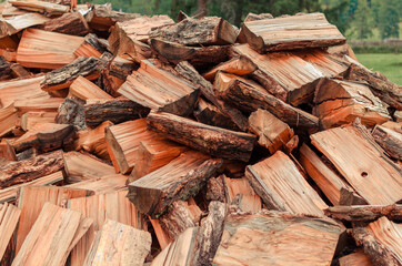 Firewood is stacked in autumn. Chopped pile of wood. Lots of wood from logs. Preparation of firewood for the winter. background texture pattern with stacked dry chopped firewood. Trees in the sawmill