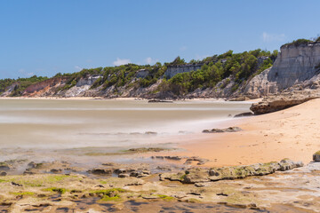 Tropical beach with reefs, yellow sand, silky sea and clear cliffs on a beautiful blue sky day.
