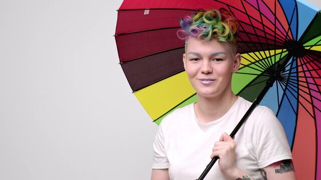 Beautiful young girl with dyed hair and a short haircut. Opens a bright colored umbrella and twists it in front of the camera.