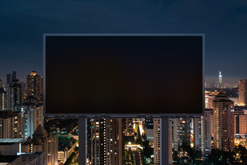Blank black road billboard with Kuala Lumpur cityscape background at night time. Street advertising poster, mock up, 3D rendering. Front view. Concept of marketing to promote or sell idea or product.