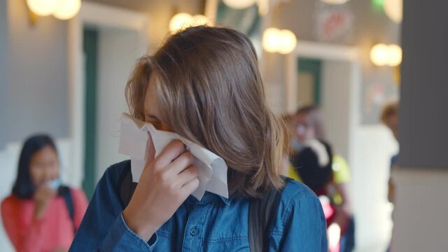 Portrait of sick caucasian teen student blowing runny nose with paper tissue