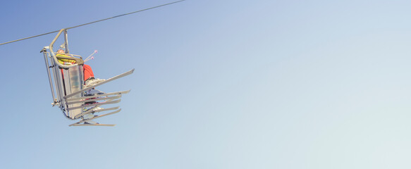 Banner with big group of skiers in ski lift, going uphill in a ski resort at blue and yellow clean gradient sky during sunset with copy space for text.