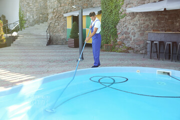Worker cleaning outdoor swimming pool with underwater vacuum