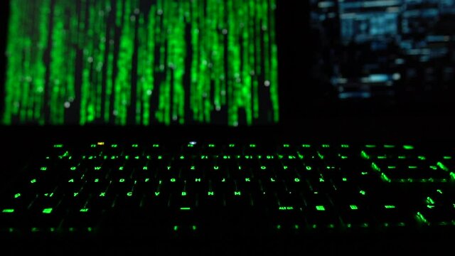 Cybersecurity concept. Hacker code on two computer screens with green lit keyboard infront