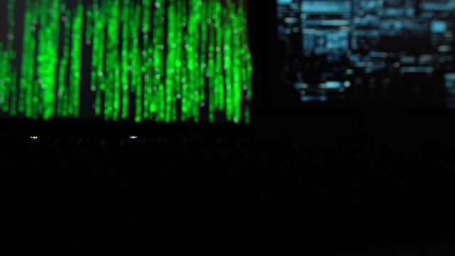 Cybersecurity concept. Hacker code on changing colors on two computer screens with green blinking keyboard infront