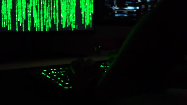 Cybersecurity concept. Slowmotion of hacker entering code on green lit keyboard, hacker code in the background