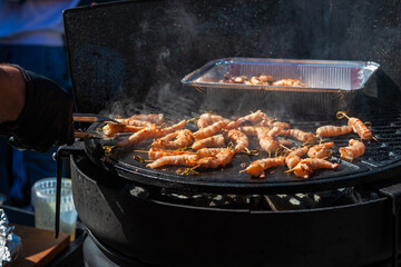 A professional cook prepares shrimps on the grill outdoor, food or catering concept