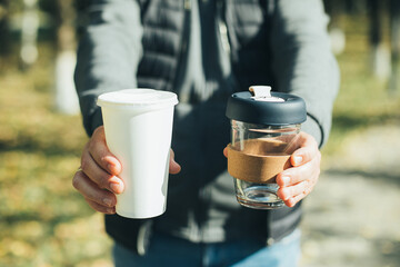 Men holding takeaway coffee cup and disposable paper cup with plastic lid. Conscious choice