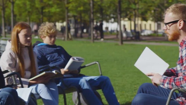 Young male teacher and diverse preteen students sitting in autumn park studying outdoors