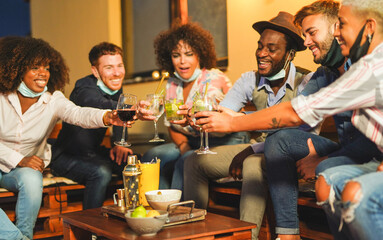 Multiracial friends cheering with cocktails outdoor while wearing surgical face mask under chin - Coronavirus lifestyle