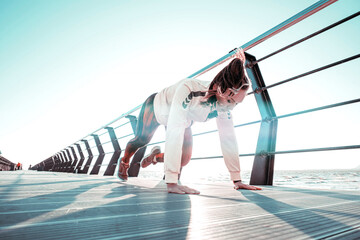 outdoor workout concept. young woman in tracksuit performs sports workout on the pier