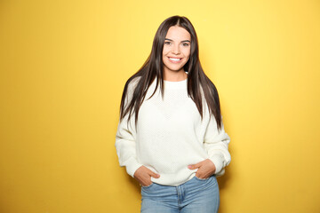 Happy young woman wearing warm sweater on yellow background