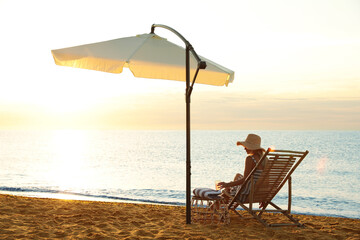 Woman with cocktail relaxing on deck chair at sandy beach. Summer vacation