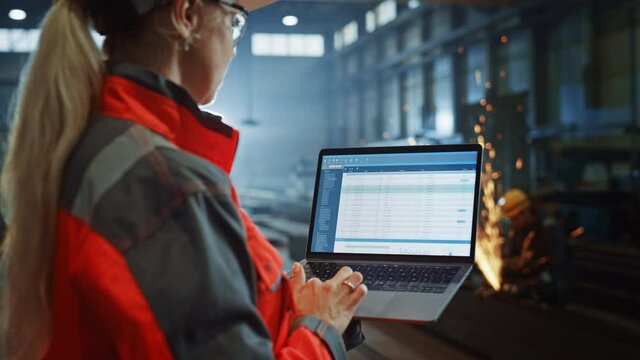 Professional Heavy Industry Engineer Uses Laptop Computer with Administrative Data Cataloging Software. Female Industrial Specialist Working in a Metal Manufacture Warehouse.