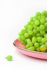 Green grapes on pink plate on white background vertical with copy space. Side view.