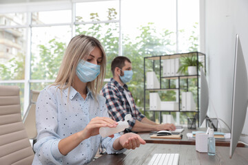 Office employee in mask applying hand sanitizer at workplace