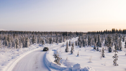 Bird’s eye view of vehicle car moving on rural road having good insurance for winter weather, aerial view of suv automobile driving in scenery area surrounded by coniferous forest.