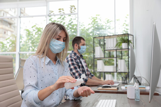 Office Employee In Mask Applying Hand Sanitizer At Workplace