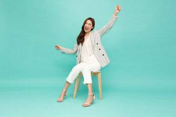 Fototapeta na wymiar Attractive beautiful Asian woman sitting on white modern chair and hands up raised arms from happiness, Excited businesswoman winner success concept